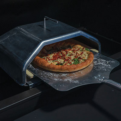 Pizza baking accessory for Green Mountain Grills, featuring a pizza stone and metal cover, showcasing a freshly baked pizza with toppings.