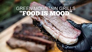 Close-up of a hand holding a slice of brisket, showcasing juicy texture, with "Green Mountain Grills" and "Food is Mood" text overlay, highlighting grilling and cooking themes.