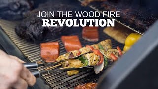Grilling vegetables and meats on a Green Mountain Grill, with text overlay "JOIN THE WOOD FIRE REVOLUTION."