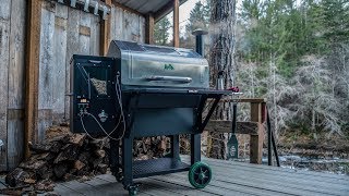 Green Mountain Grills pellet grill on a wooden deck, surrounded by trees, showcasing its design and functionality for outdoor cooking.
