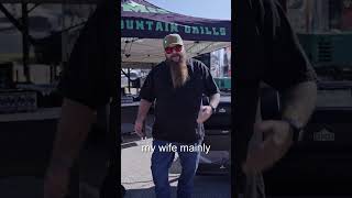 Man in sunglasses and a black shirt standing in front of a Green Mountain Grills tent, discussing pellet grilling.