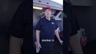 Man in a Green Mountain Grills shirt demonstrating a pellet smoker in a barbecue setup, highlighting grilling techniques and equipment.