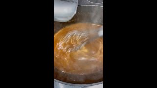 Cooking pot with smoky BBQ sauce being stirred, showcasing the preparation process for flavorful dishes like pulled pork or brisket.